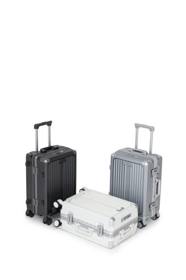 Drei Koffer in verschiedenen Farben: Schwarz, Grau und Weiß, mit Rollen und Griffen.